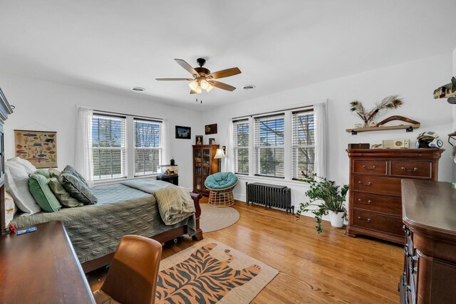 bedroom featuring multiple windows, light wood-style flooring, a ceiling fan, and radiator