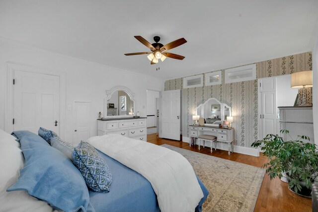 bedroom featuring ceiling fan, baseboards, wood finished floors, and wallpapered walls