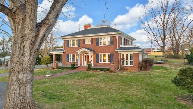 colonial-style house with a front lawn, a chimney, and brick siding