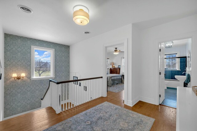 corridor with visible vents, wood finished floors, an upstairs landing, and wallpapered walls