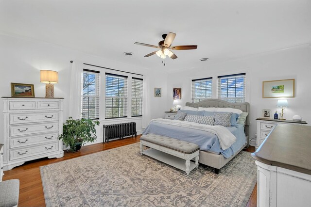 bedroom with radiator, wood finished floors, and a ceiling fan