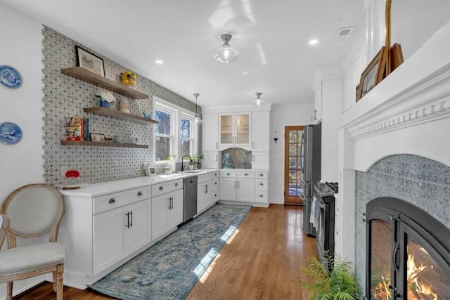 kitchen featuring white cabinets, a warm lit fireplace, a sink, light wood-type flooring, and appliances with stainless steel finishes
