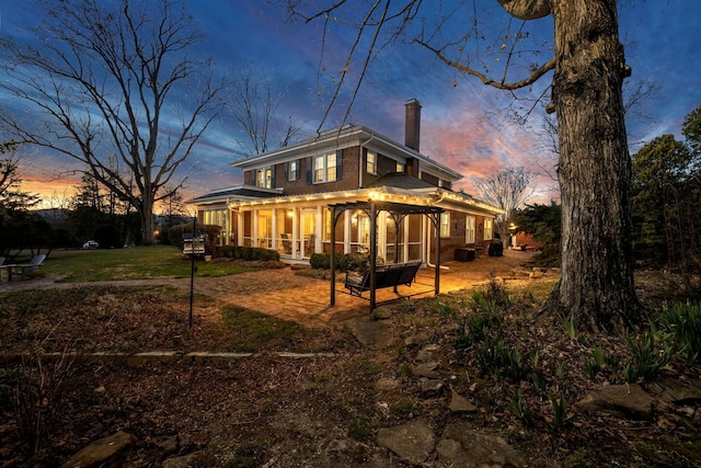 back of house at dusk featuring a chimney, a sunroom, and a lawn