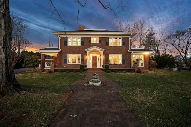 view of front of home featuring a chimney, brick siding, and a front yard