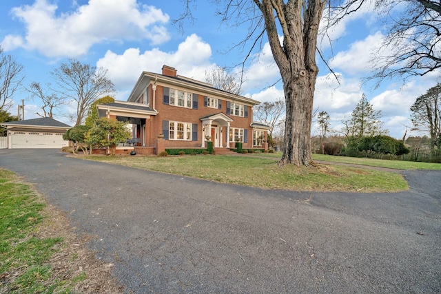 colonial house featuring a chimney, a front lawn, brick siding, and a garage