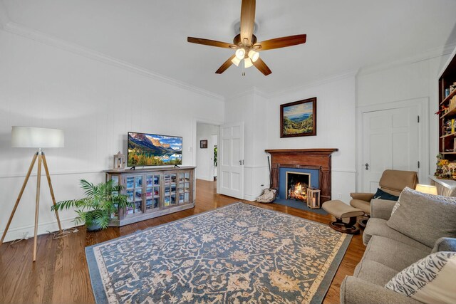 living area featuring a fireplace with flush hearth, ceiling fan, crown molding, and wood finished floors