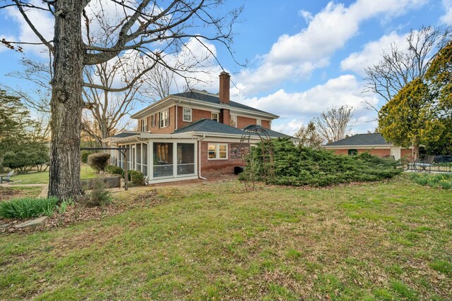 rear view of property featuring brick siding, a sunroom, a chimney, and a lawn