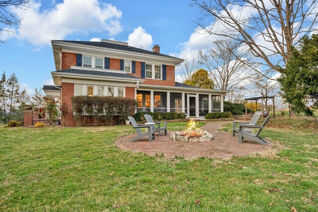 back of house featuring a chimney, brick siding, a patio, an outdoor fire pit, and a sunroom