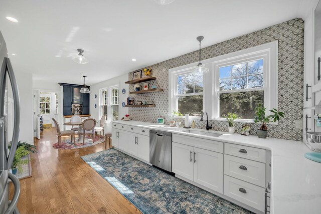kitchen featuring a sink, white cabinetry, wood finished floors, appliances with stainless steel finishes, and hanging light fixtures