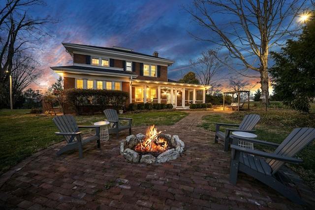 rear view of house featuring a chimney, brick siding, a patio area, a sunroom, and an outdoor fire pit