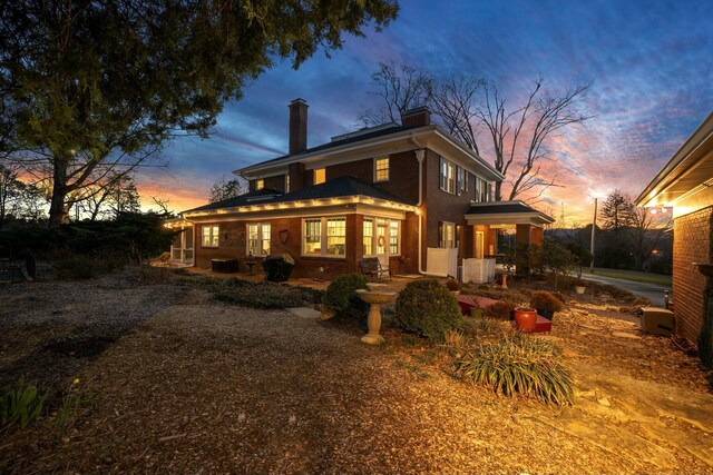 back of property at dusk with a chimney and brick siding