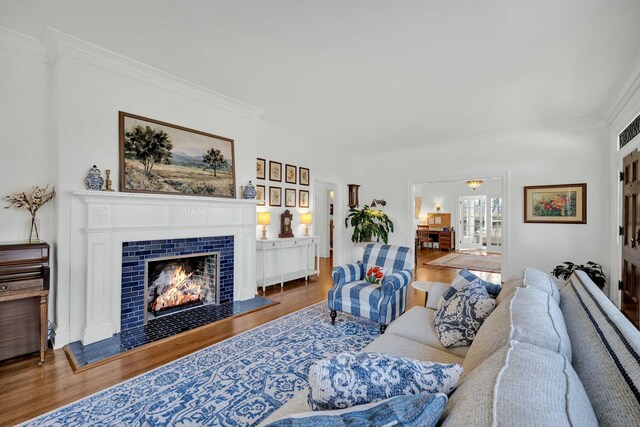 living room featuring a tile fireplace, ornamental molding, and wood finished floors