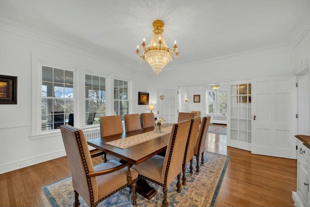 dining space with crown molding, radiator heating unit, wood finished floors, a chandelier, and baseboards