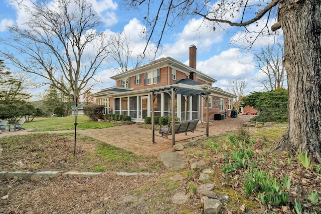 back of house with brick siding, a patio area, a sunroom, and a chimney