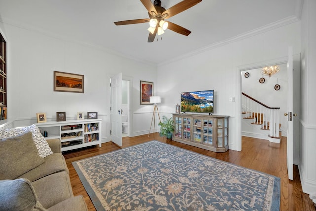 living room with baseboards, ceiling fan with notable chandelier, wood finished floors, stairway, and crown molding