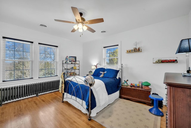bedroom featuring radiator, visible vents, light wood finished floors, and ceiling fan
