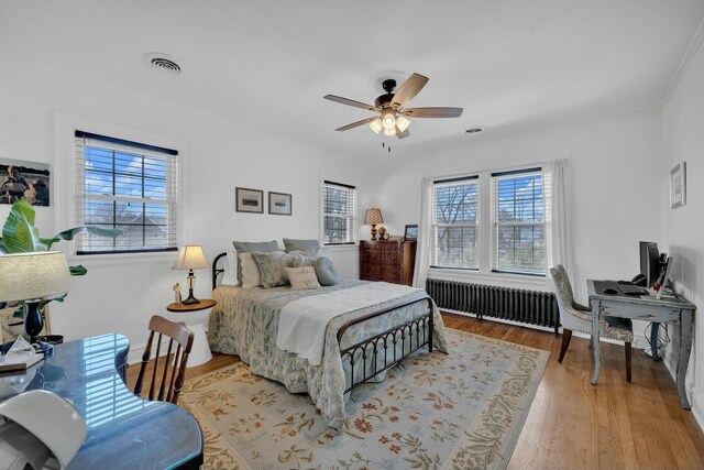 bedroom with a ceiling fan, radiator heating unit, wood finished floors, and visible vents