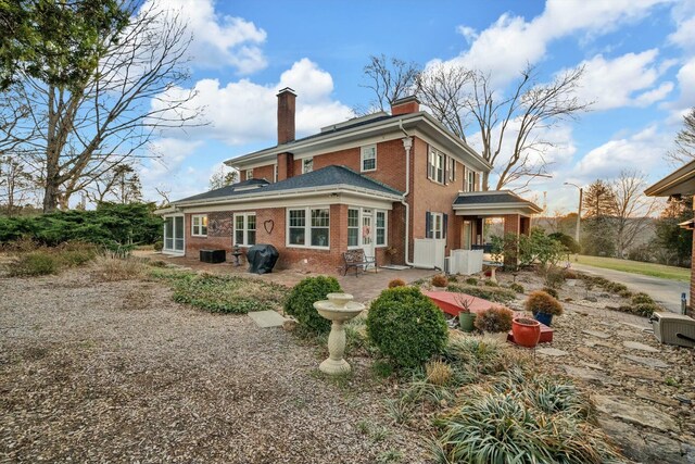 rear view of property with brick siding, a patio area, and a chimney