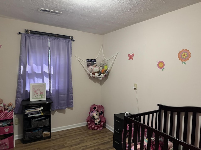 bedroom featuring a textured ceiling, a nursery area, and dark hardwood / wood-style floors