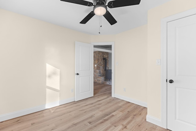 unfurnished bedroom featuring a wood stove, ceiling fan, and light hardwood / wood-style flooring