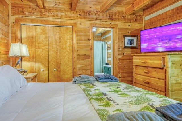 bedroom with wooden walls, beamed ceiling, a closet, and wood ceiling