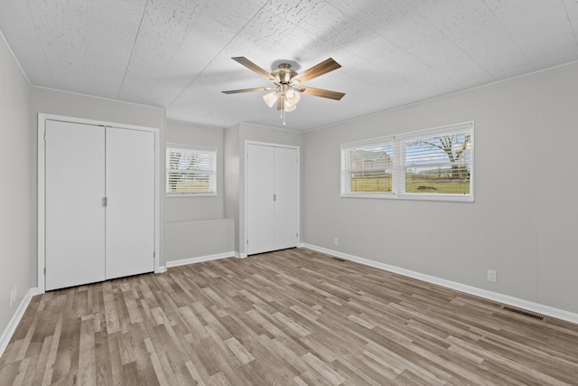 unfurnished bedroom featuring multiple closets, ceiling fan, and light hardwood / wood-style flooring