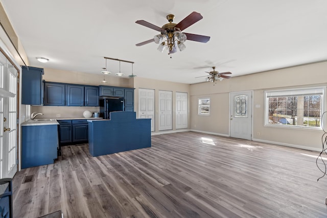 kitchen featuring black refrigerator, light wood-type flooring, blue cabinetry, a kitchen island, and pendant lighting