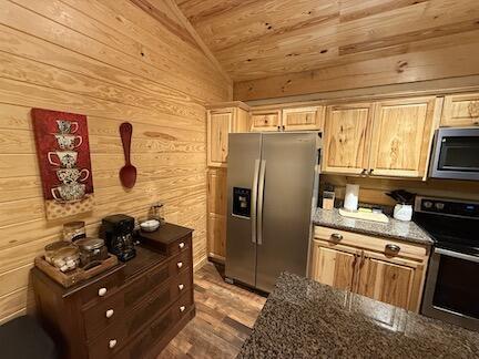 kitchen featuring wood walls, dark stone counters, vaulted ceiling, wood ceiling, and appliances with stainless steel finishes