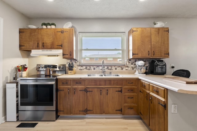 2121 Fir St, Morristown, TN 37813 - kitchen with under cabinet range hood, stainless steel electric range oven, a sink, backsplash, and brown cabinetry