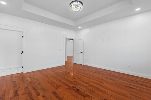 empty room featuring hardwood / wood-style floors, a notable chandelier, and a raised ceiling