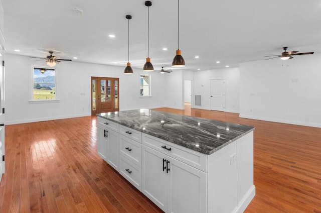 kitchen featuring dark stone counters, decorative light fixtures, hardwood / wood-style floors, a center island, and white cabinetry