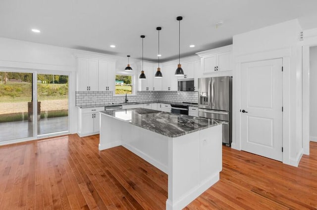 kitchen featuring appliances with stainless steel finishes, light wood-type flooring, tasteful backsplash, a kitchen island, and white cabinetry