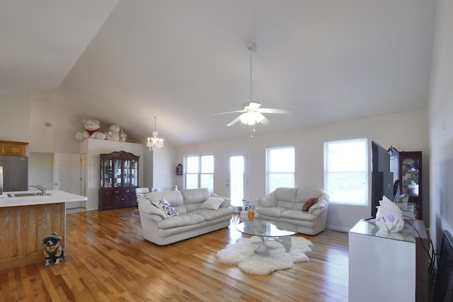 living room with ceiling fan with notable chandelier, light hardwood / wood-style floors, vaulted ceiling, and sink