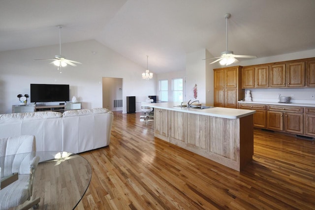 kitchen featuring lofted ceiling, a kitchen island with sink, ceiling fan with notable chandelier, sink, and hardwood / wood-style flooring