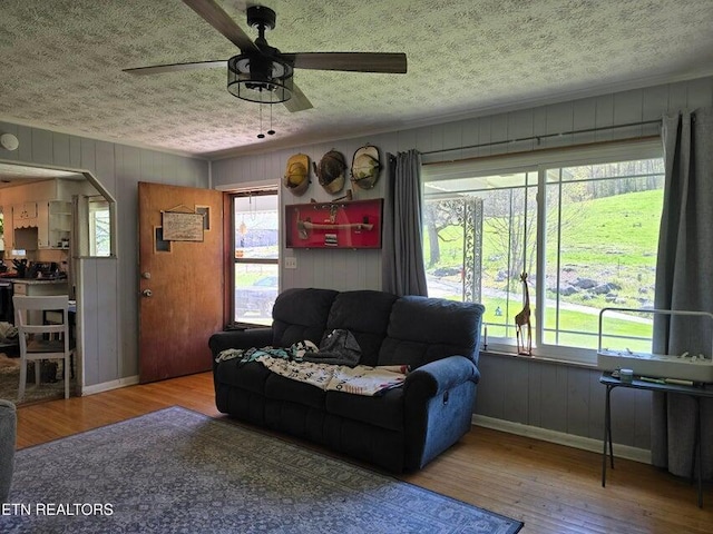living room with a textured ceiling, wood finished floors, a ceiling fan, and baseboards