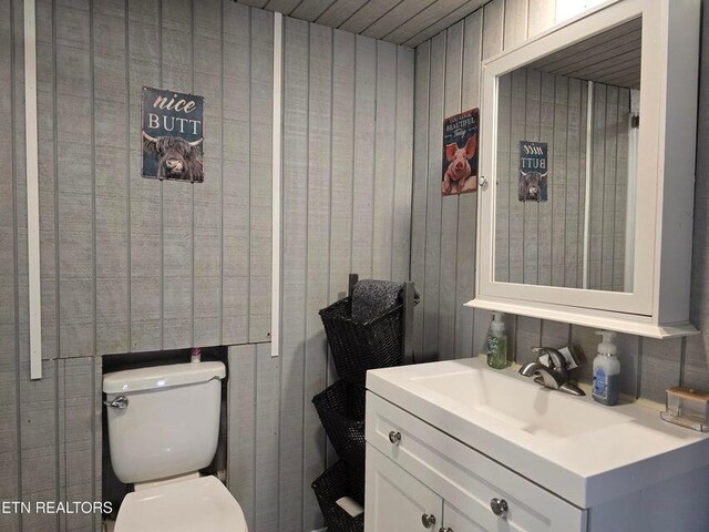 half bathroom featuring toilet, wooden walls, and vanity