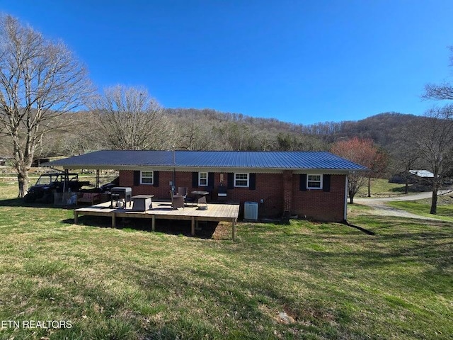 back of property with a deck with mountain view, brick siding, metal roof, cooling unit, and a lawn