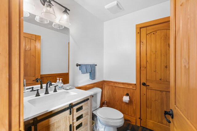 bathroom featuring vanity, toilet, and wooden walls