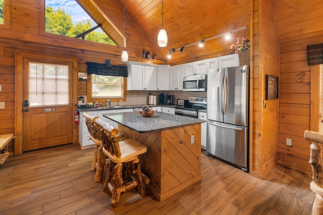 kitchen with a kitchen island, white cabinetry, stainless steel appliances, and wooden walls