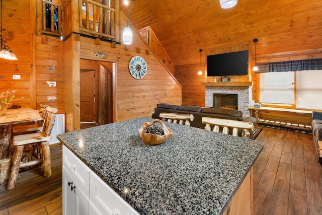 kitchen featuring a kitchen island, dark stone countertops, wood walls, decorative light fixtures, and white cabinets