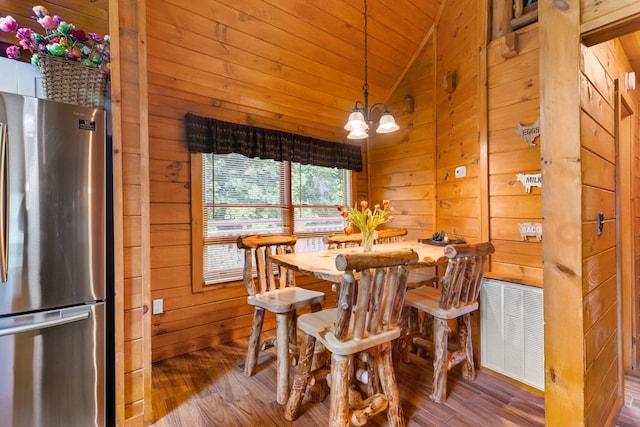 dining room with a chandelier, wooden walls, wood-type flooring, and vaulted ceiling