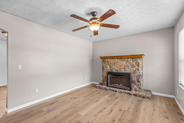 unfurnished living room featuring a stone fireplace, ceiling fan, a textured ceiling, and light wood-type flooring