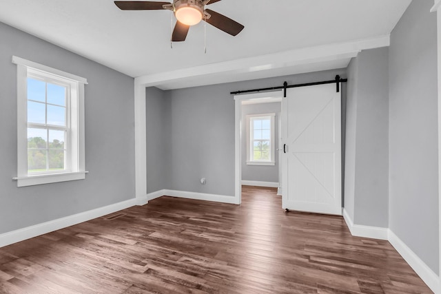 unfurnished room featuring ceiling fan, a barn door, and dark hardwood / wood-style flooring