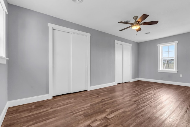 unfurnished bedroom with ceiling fan, wood-type flooring, and two closets