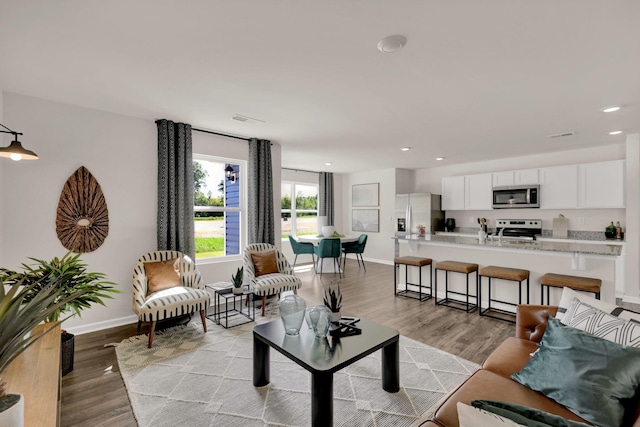 living room with light wood-style flooring, visible vents, baseboards, and recessed lighting