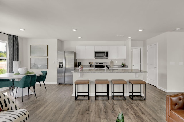 kitchen with white cabinetry, appliances with stainless steel finishes, a breakfast bar, and wood finished floors