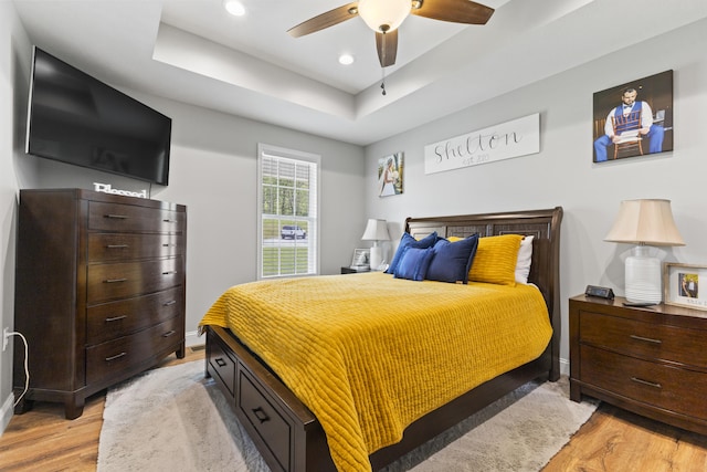 bedroom featuring a ceiling fan, a tray ceiling, light wood-style flooring, baseboards, and recessed lighting