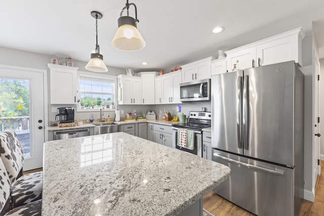 kitchen featuring a sink, decorative light fixtures, light stone countertops, appliances with stainless steel finishes, and white cabinetry