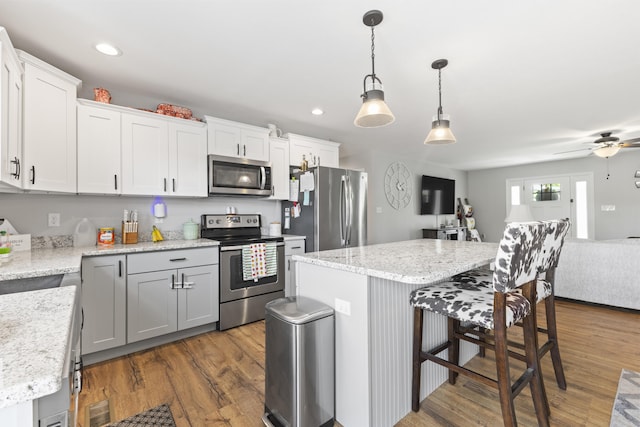 kitchen with dark wood-style floors, a ceiling fan, appliances with stainless steel finishes, a breakfast bar area, and hanging light fixtures