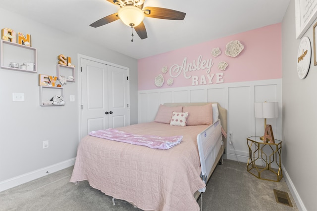 carpeted bedroom featuring a ceiling fan, visible vents, a closet, and a wainscoted wall